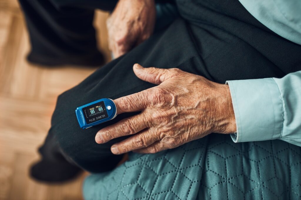 Senior man measuring the degree of oxygen saturation of the blood and heart rate at home using pulse oximeter. Home treatment of virus. Checking health condition. Coronavirus pandemic. Covid 19 outbreak